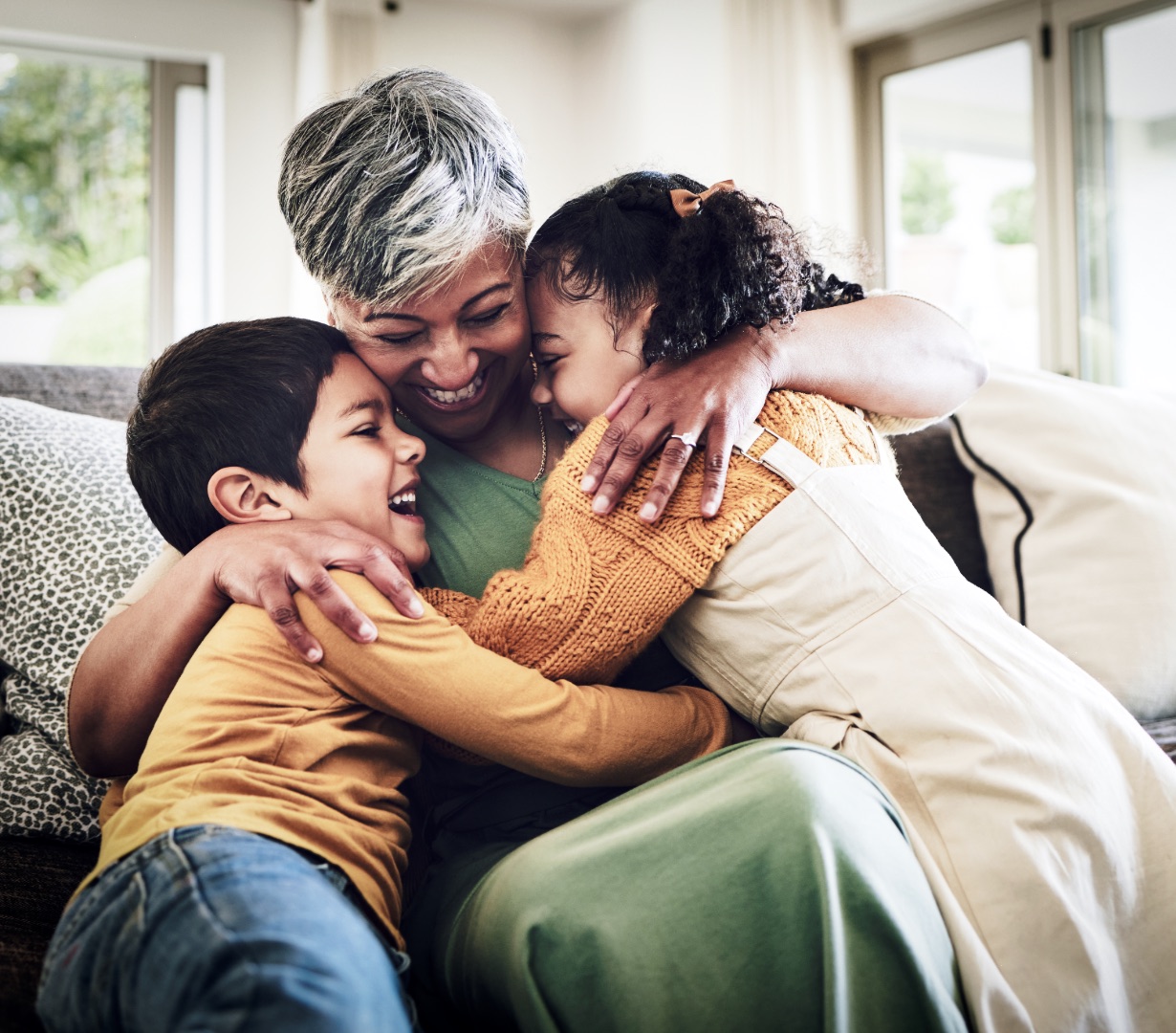 A grandmother embracing two laughing grandchildren at home