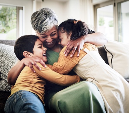 A grandmother embracing two laughing grandchildren at home