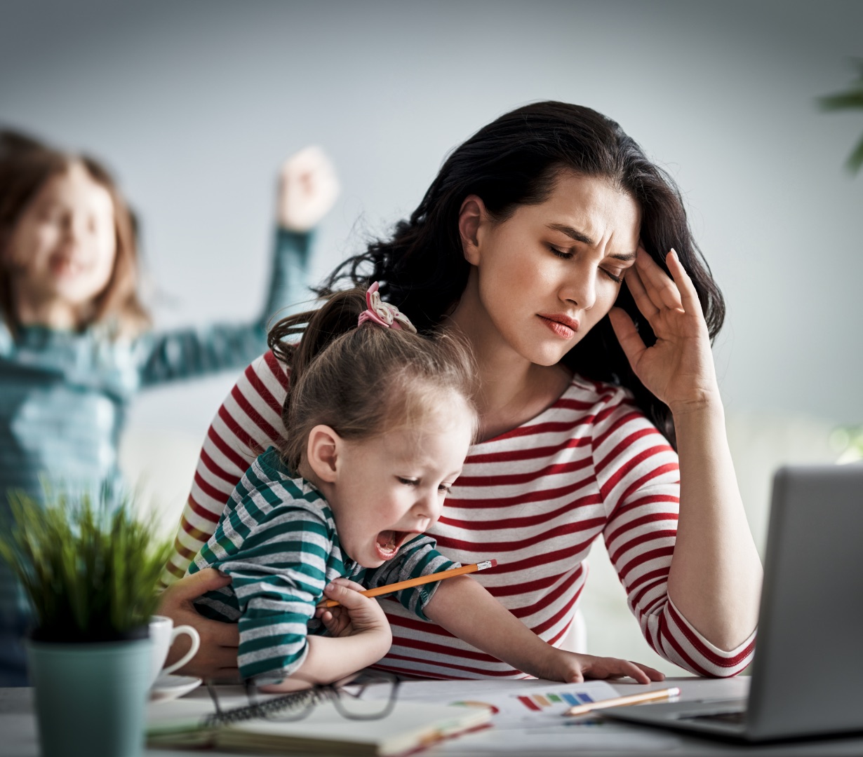 A parent holding their children while working, carrying the mental load